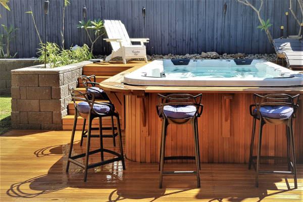A large spa pool with a bespoke wooden surround including steps and wrap-around bar with stools.